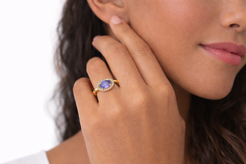 Close-up of a woman wearing a gold ring with a purple gemstone on her finger.